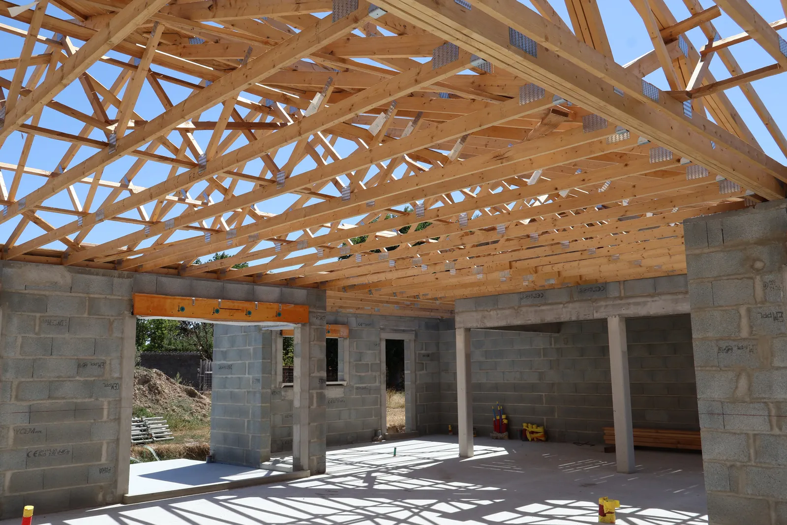 Chantier de maison en cours, murs de maçonnerie montés et charpente posée.