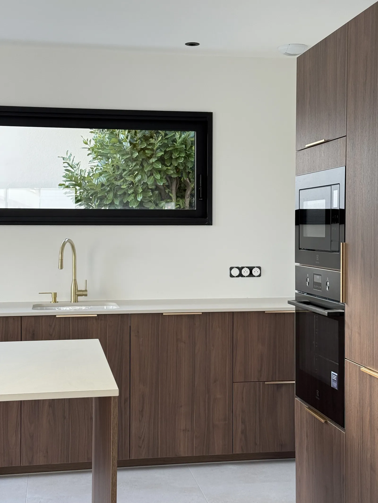 Cuisine ouverte d'une maison neuve, façades bois foncé, robinetterie laitonnée et four encastré.
