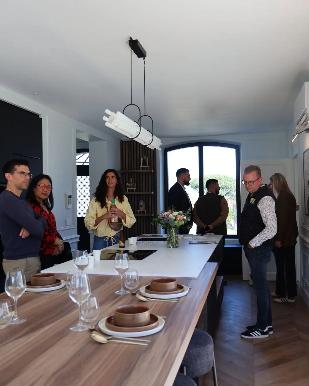 Visiteurs dans la cuisine ouverte, autour de l'îlot dressé de verres et de bols en bois.
