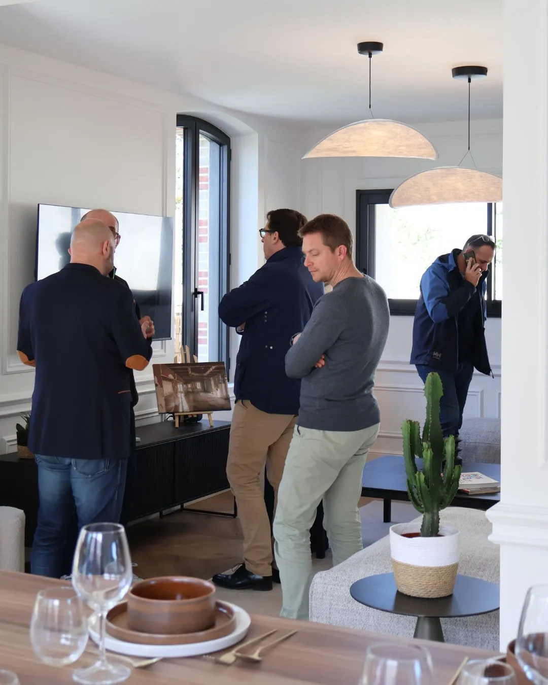 Trois visiteurs discutent dans le salon lumineux, sous des suspensions en papier.