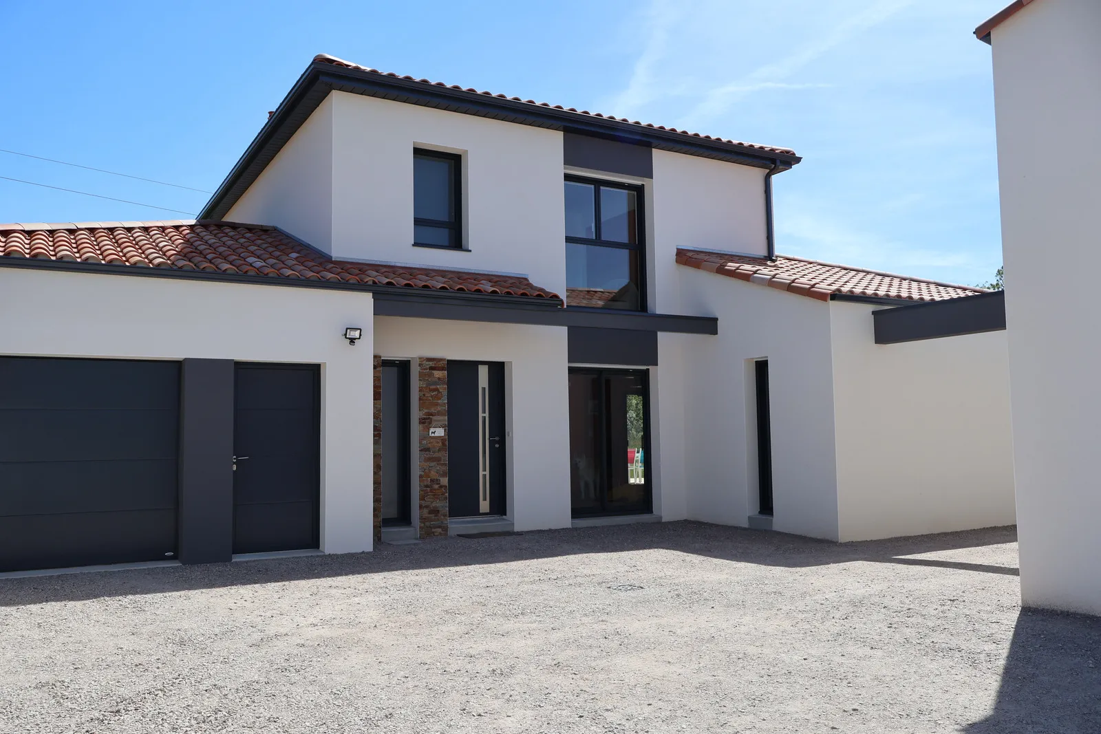 Façade d'une maison moderne à étage, enduit clair et toiture en tuiles, vue depuis l'allée.