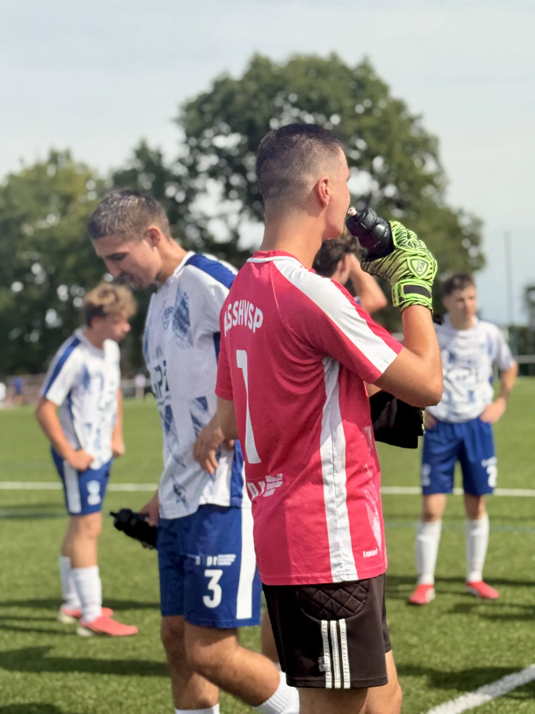 Le gardien de l'ASSHVSP, en maillot rose, boit une gorgée au milieu de ses coéquipiers en blanc et bleu.