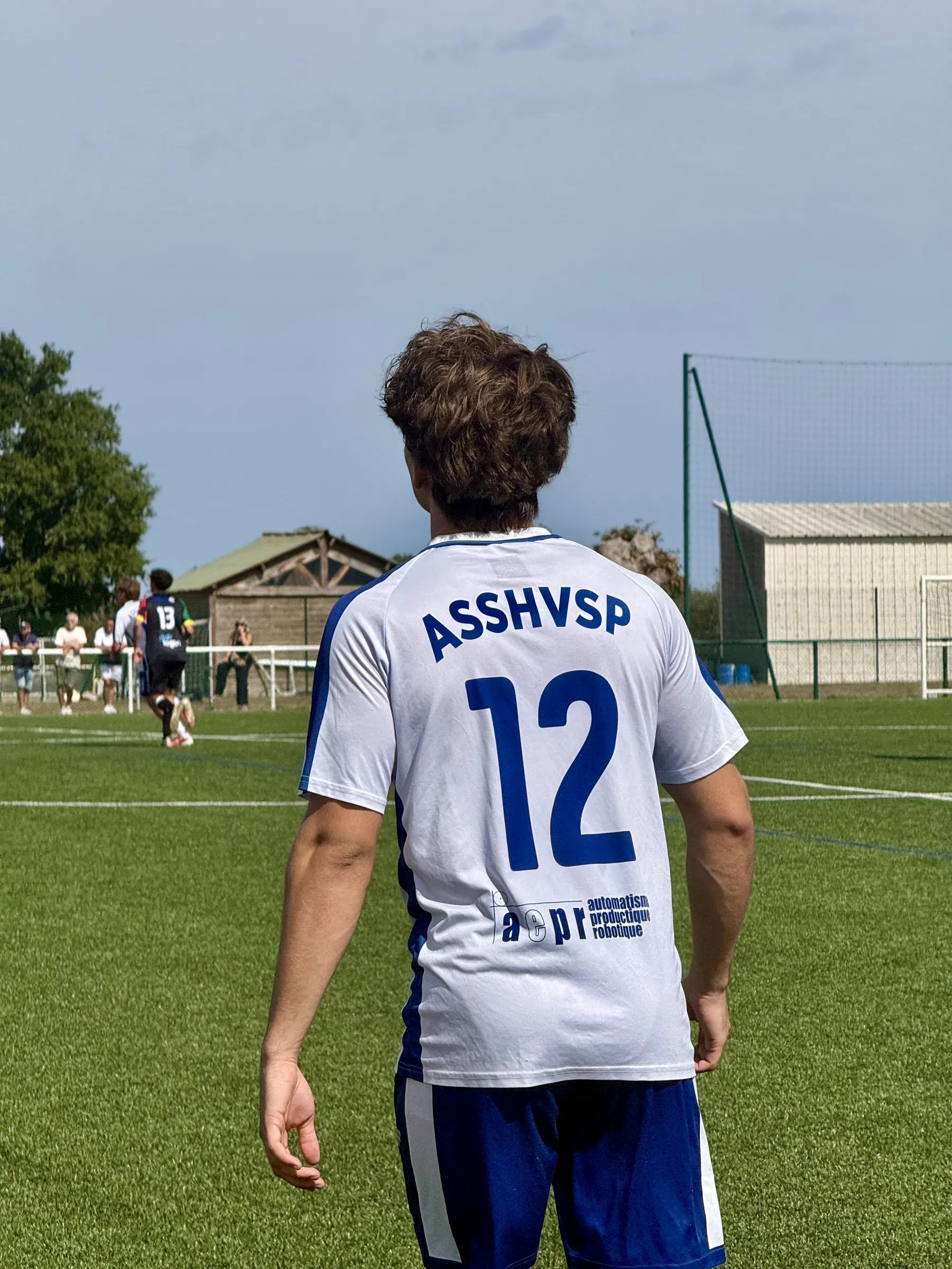 Le numéro 12 de l'ASSHVSP, de dos, regarde le jeu sur un terrain synthétique.