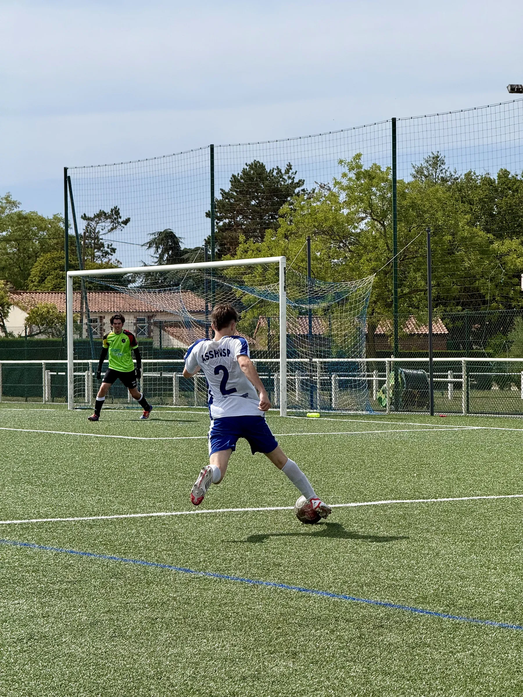Un joueur frappe le ballon vers le but, où le gardien se tient prêt.
