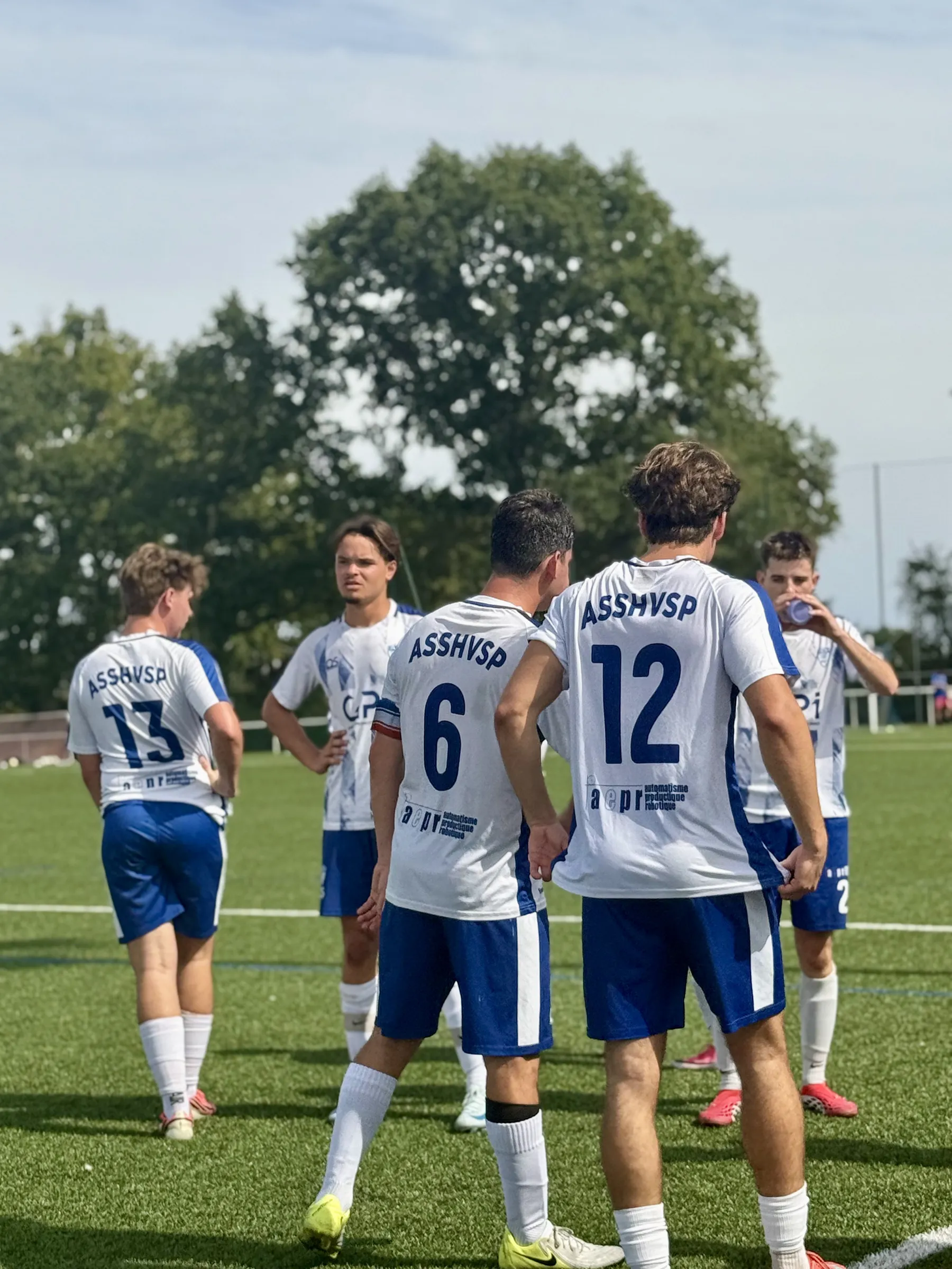 Des joueurs discutent en groupe sur la pelouse, avant la reprise.