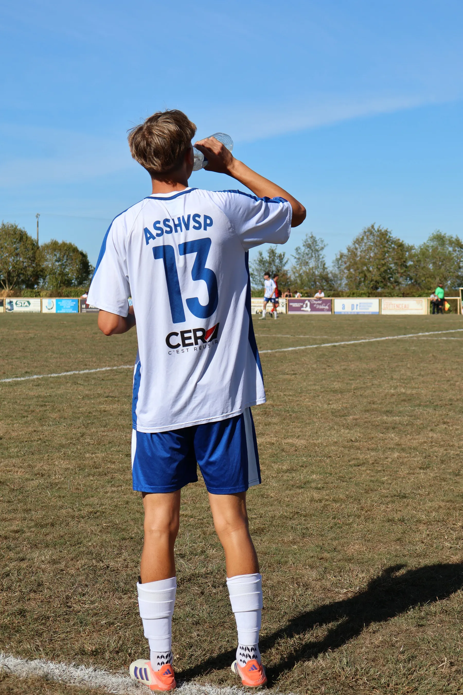 Le numéro 13 de l'ASSHVSP, de dos, boit une gorgée d'eau au bord du terrain.